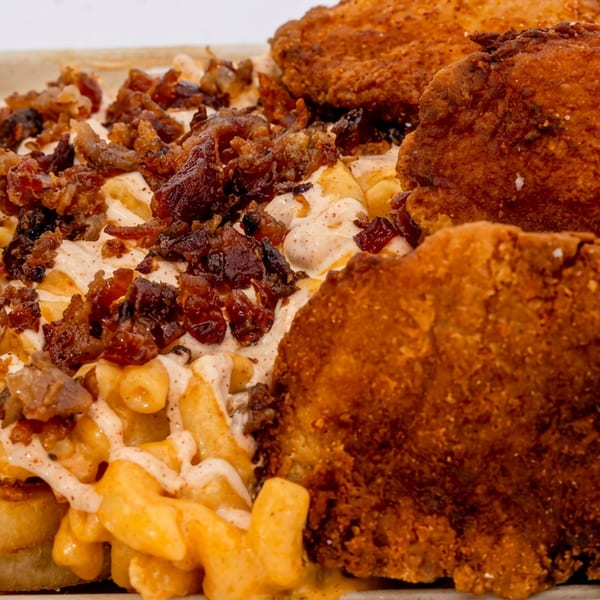 Crispy fried chicken pieces and macaroni and cheese topped with bacon bits and sauce.