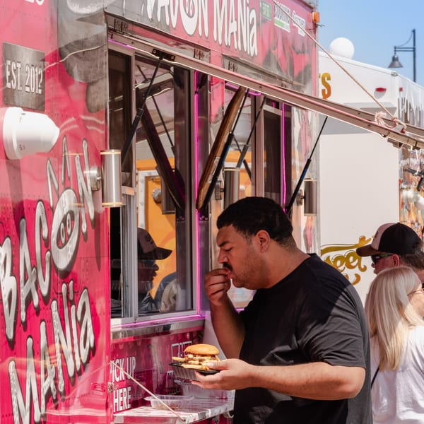 Man eating a burger and fries from the "Bacon Mania" food truck.
